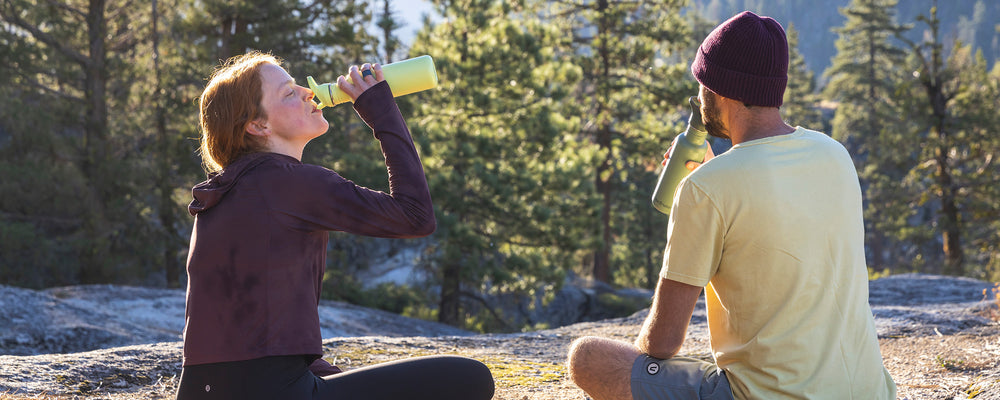 Man and woman drinking from sports water bottles - outside doing yoga