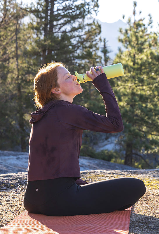 Woman drinking from sports water bottle - outside doing yoga